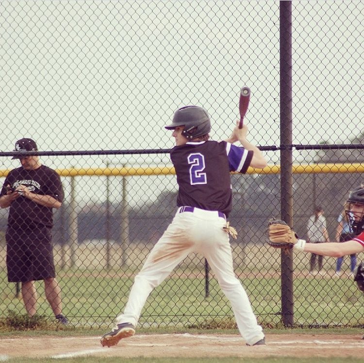 A batter in a black and purple jersey waiting for a pitch at home plate