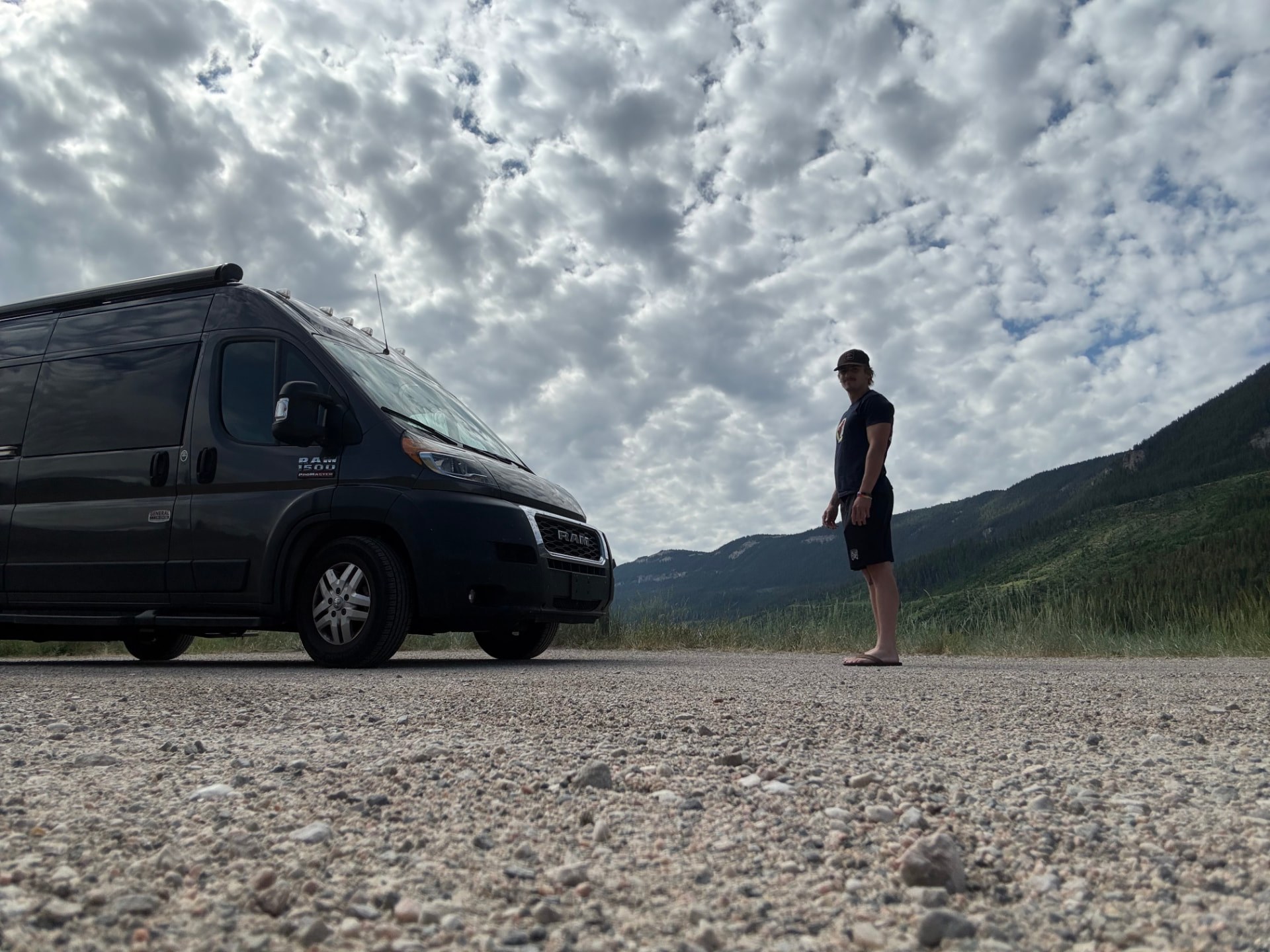 Michael standing beside the Road2Victory van on a gravel road above forested hills