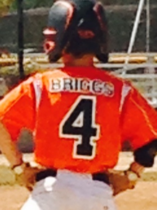 A player in a Road2Victory jersey standing on a baseball field with purple flowers in bloom